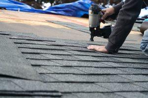 handyman using nail gun to install shingle to repair roof